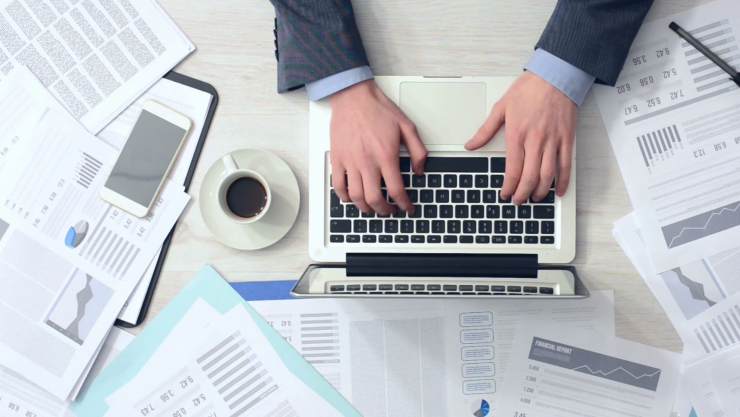 businessman-working-at-office-desk-with-his-laptop-and-drinking-coffee-surrounded-by-a-lot-of-paperwork-and-financial-reports-hands-top-view_hymiydoy_thumbnail-full01.png